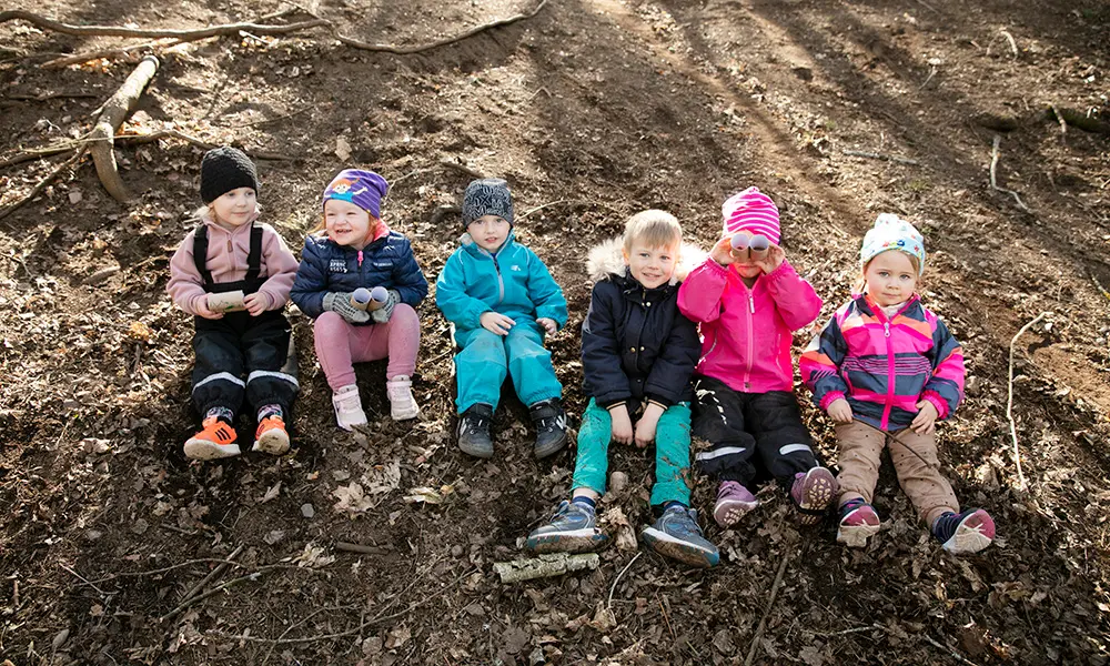 Foto av sex stycken barn som sitter bredvid varandra i en jordig backe.